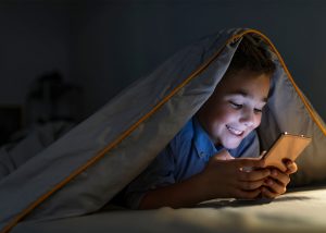 Young boy playing on his phone at night under the duvet when he should be sleeping